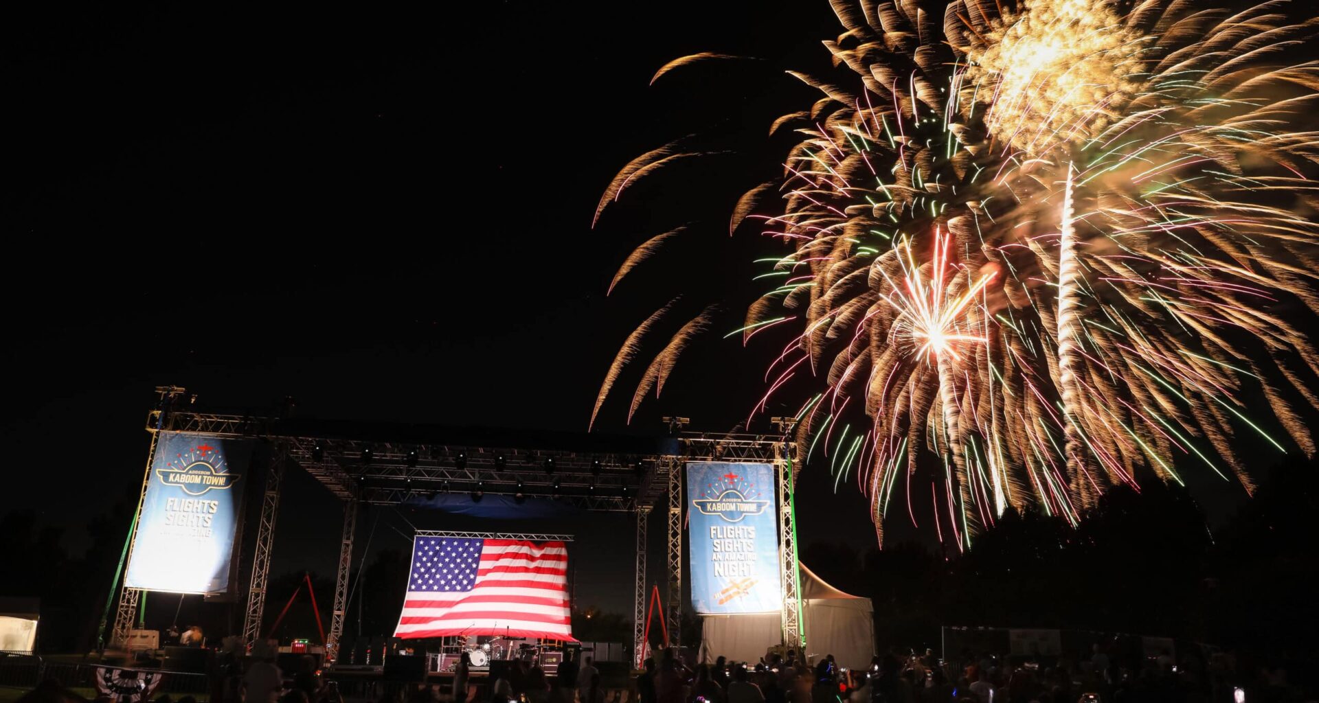 Fireworks display over outdoor stage with American flag at night.