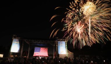 Fireworks display over outdoor stage with American flag at night.