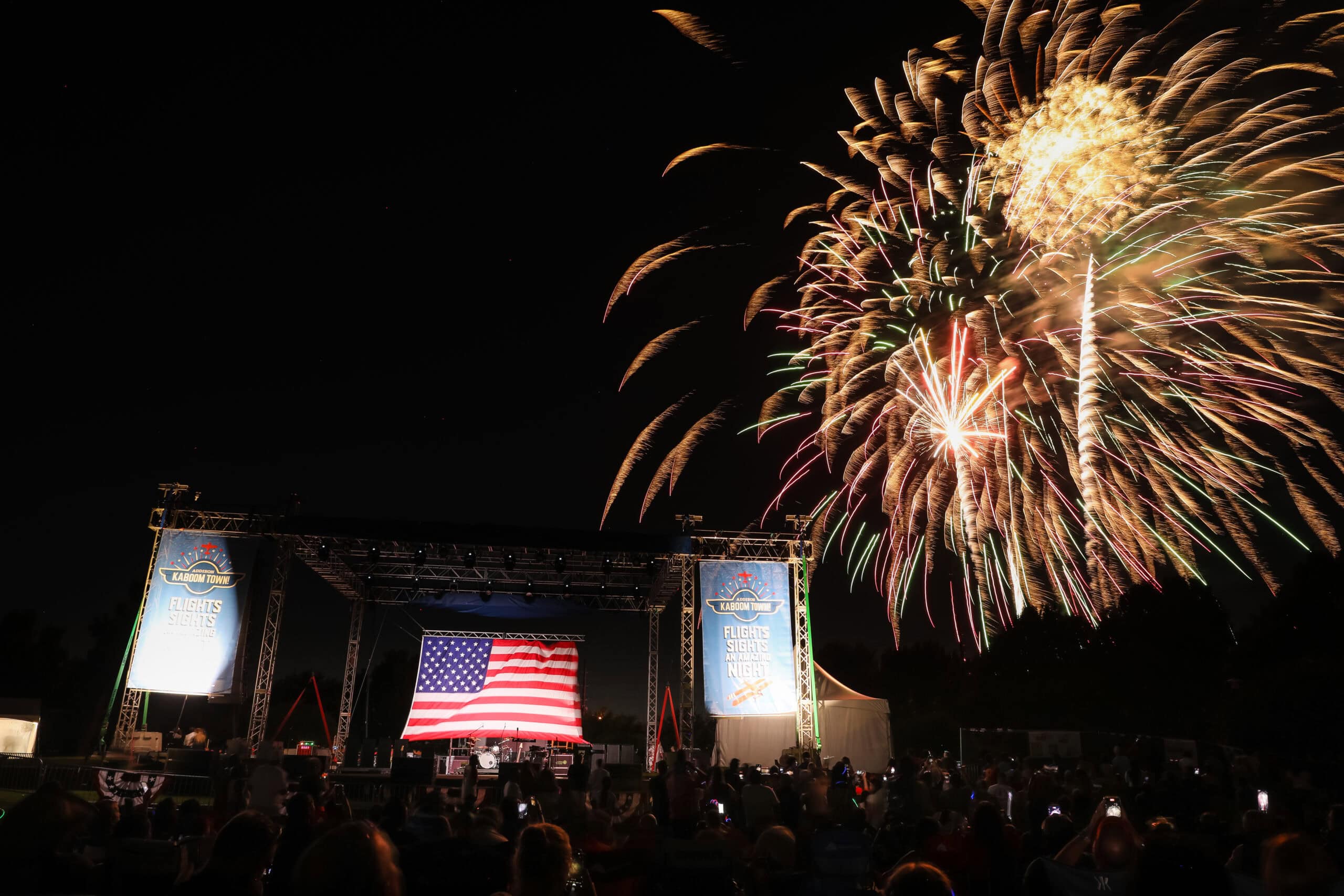 Fireworks display over outdoor stage with American flag at night.