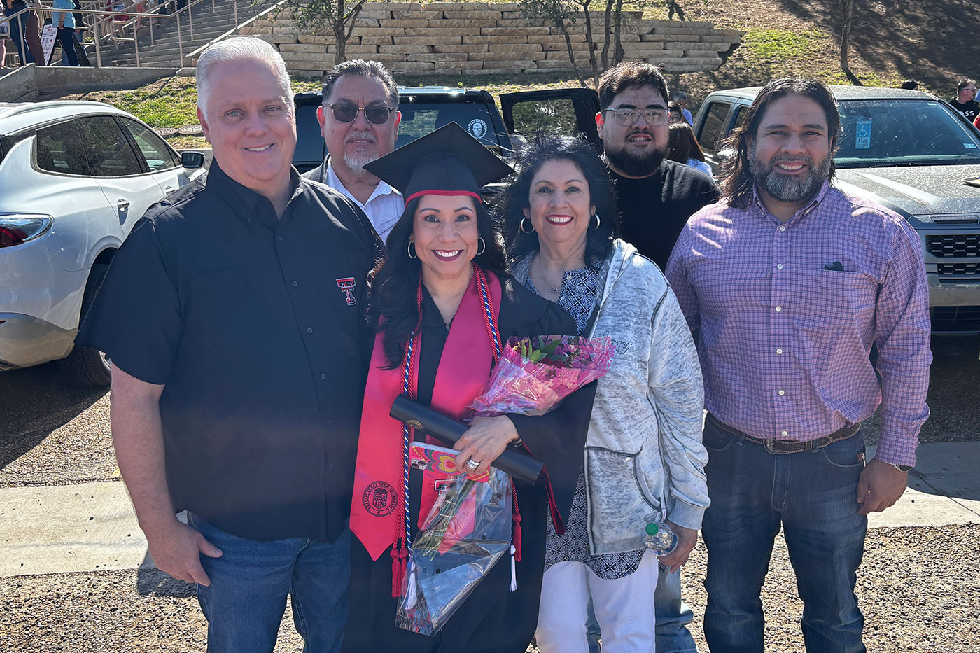 Lesley in graduation regalia holding diploma, with family group of husband, mom, brother, uncle and nephew