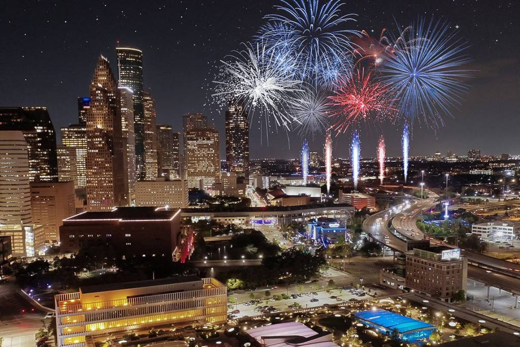 Image shows a patriotic firework show as seen from Post market in Downtown, Houston.