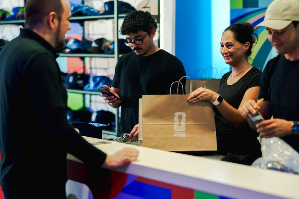 Image shows a cashier handing a package to a customer at the Official FIFA World Cup 2026 store. 
