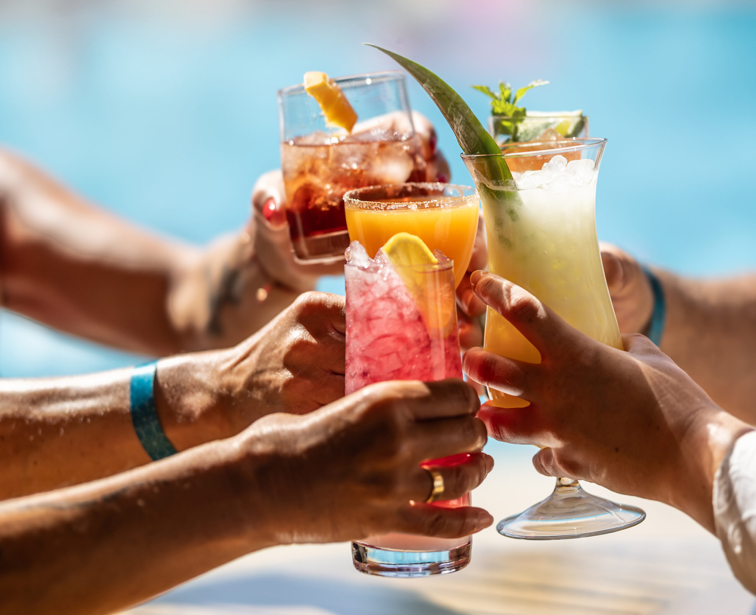 A group of guests toasts with aperitifs or cocktails by the pool at a hotel resort during their summer vacation.
