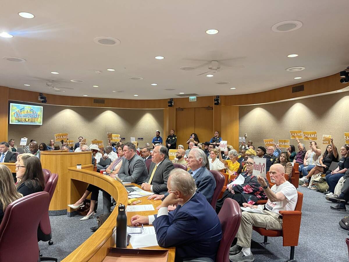 Audience at County Commissioners Court hold signs while commissioners discuss the Help Center resolution.