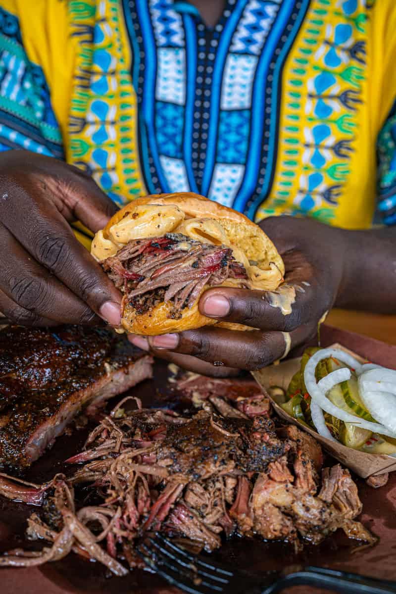 Person holding a pulled pork sandwich, colorful traditional garment