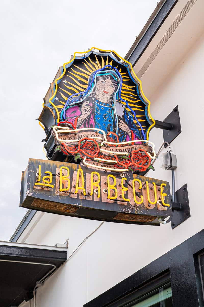 Colorful neon sign of "La Barbecue" with an illustration of a veiled figure.