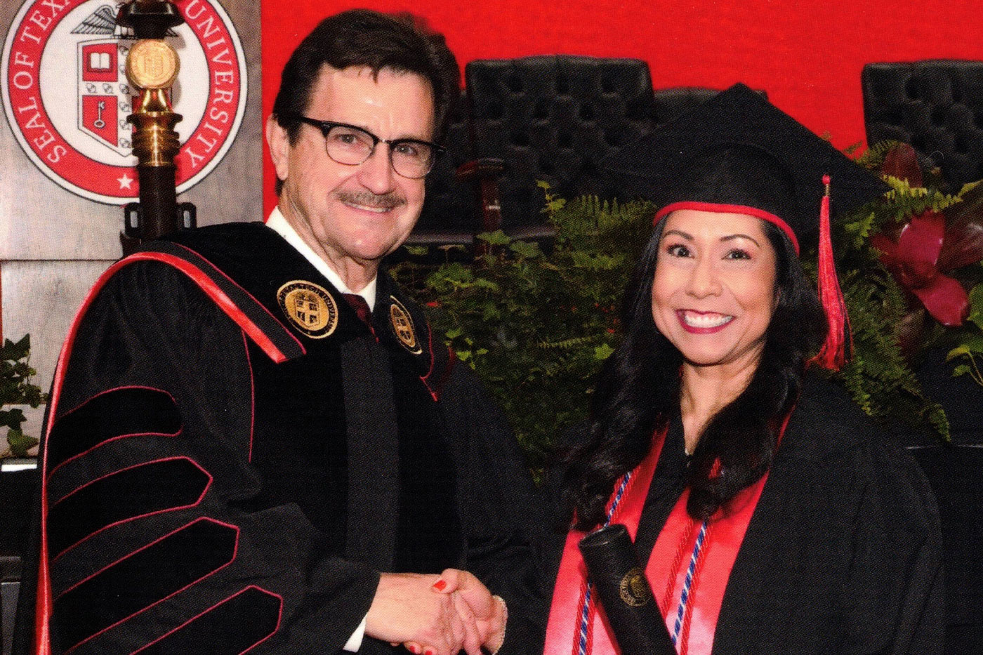 Lesley at graduation shaking hands with Texas Tech President Lawrence Schovanec