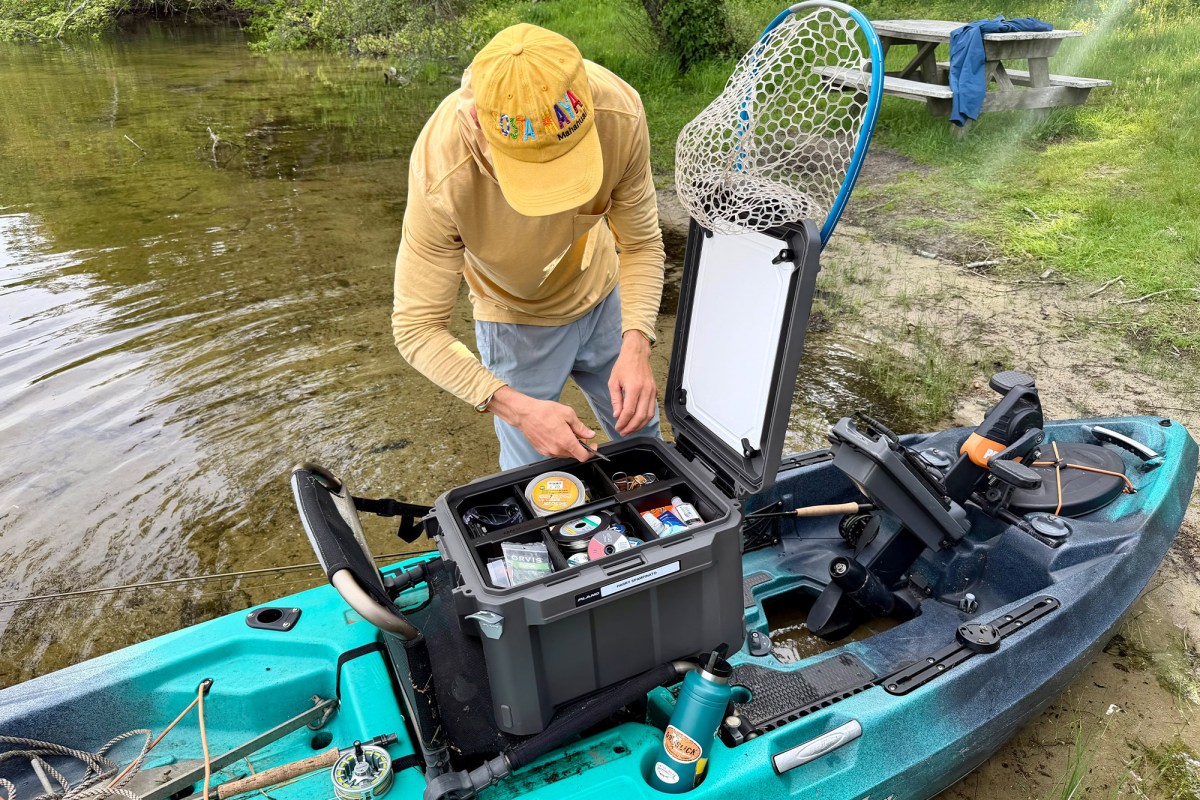 Man sorting fishing gear inside an open Plano box on a kayak