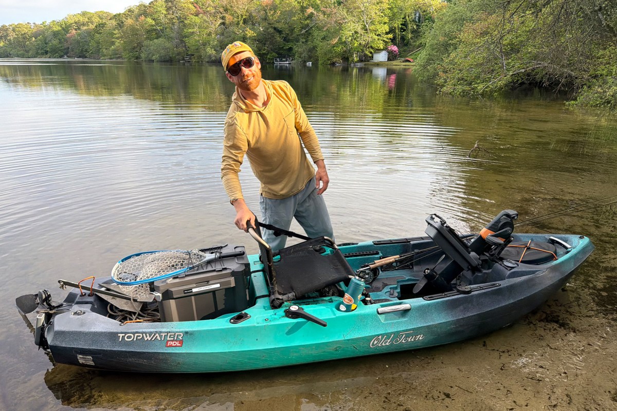 Man standing beside a kayak with a Plano box and fishing net on the back deck