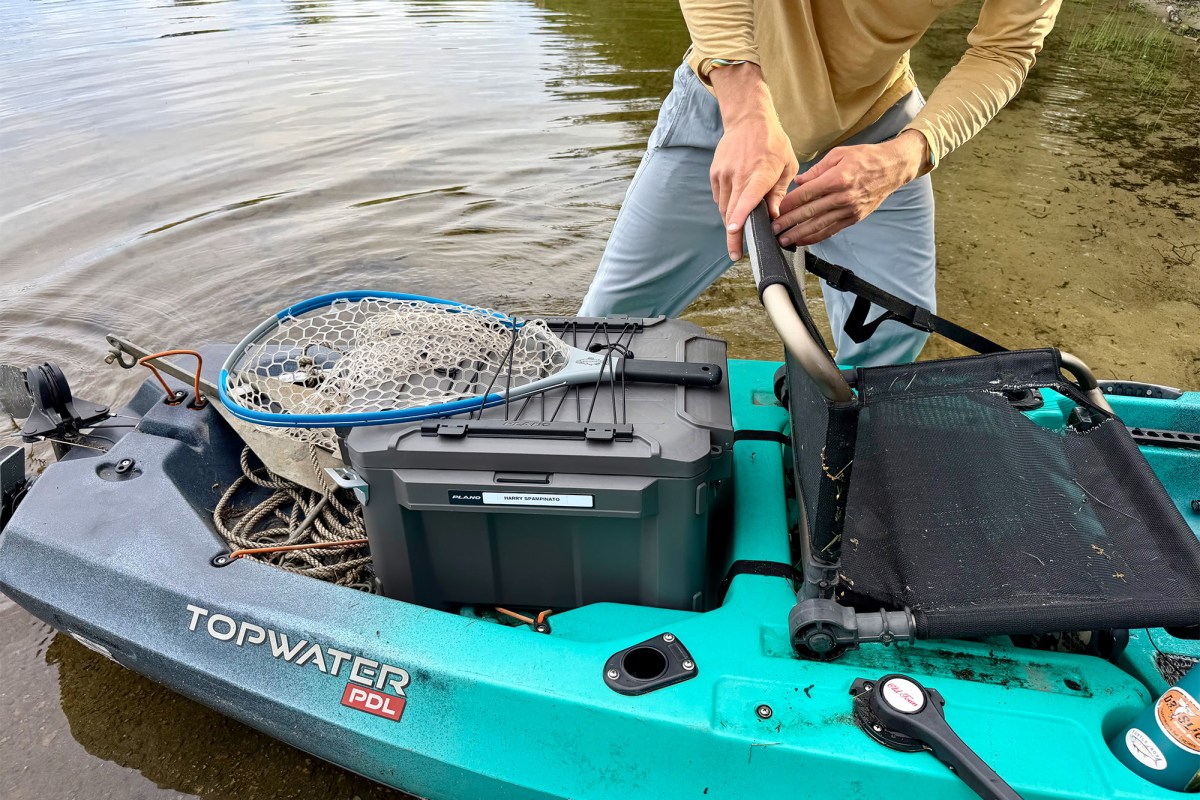 Fishing net strapped to a gray Plano box on a kayak near the water