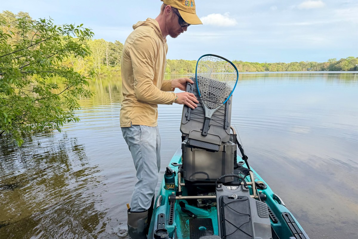 Man securing a fishing net to a Plano box on a kayak