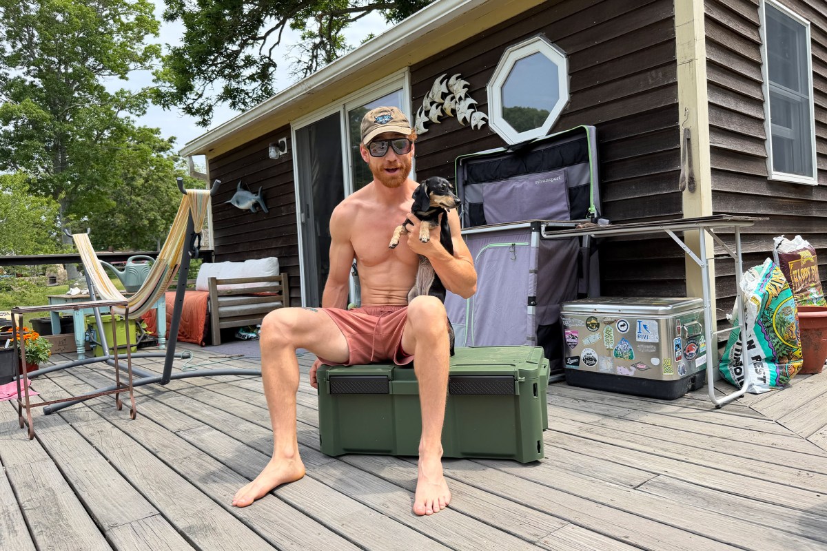 Man sitting on a green Plano box while holding a small dog