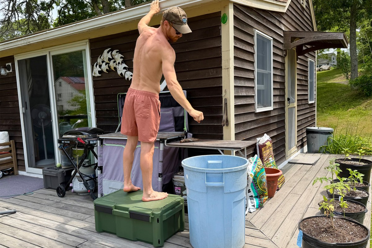 Man standing on a green storage box on a backyard deck