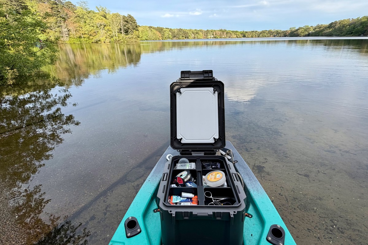 Open gear box packed with fishing supplies on the front of a kayak at the lake