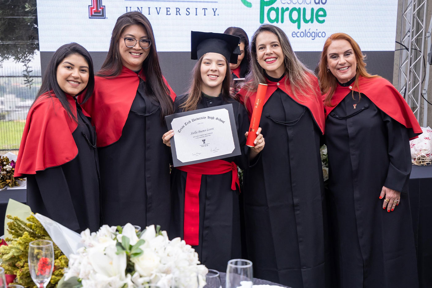 Stella Leoni poses with her diploma in the center of a group of four others, all in graduation regalia.