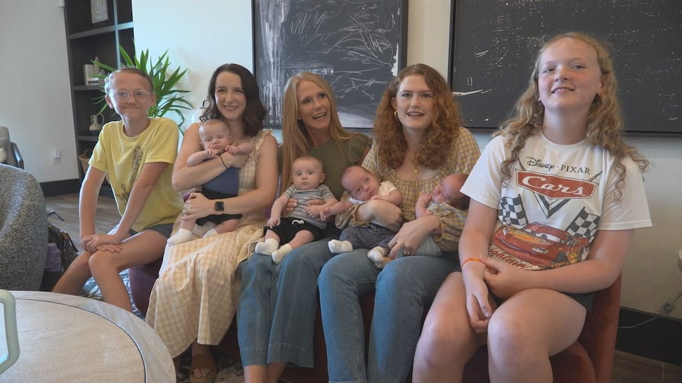 A phot of the two mothers and their family members holding all four baby boys.