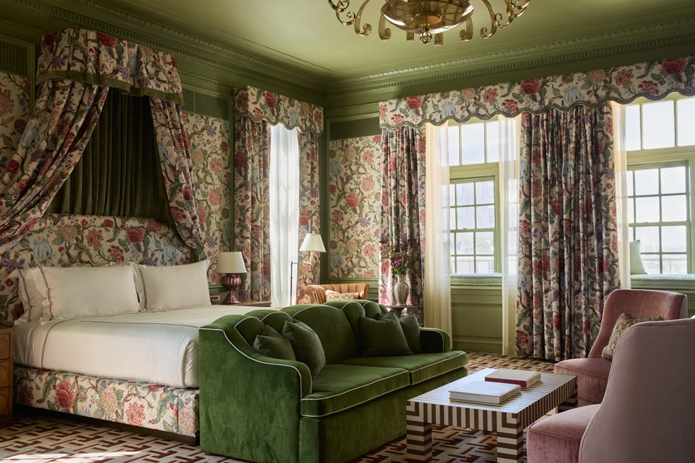 Luxurious bedroom with floral wallpaper, green velvet sofa, and pink armchairs.