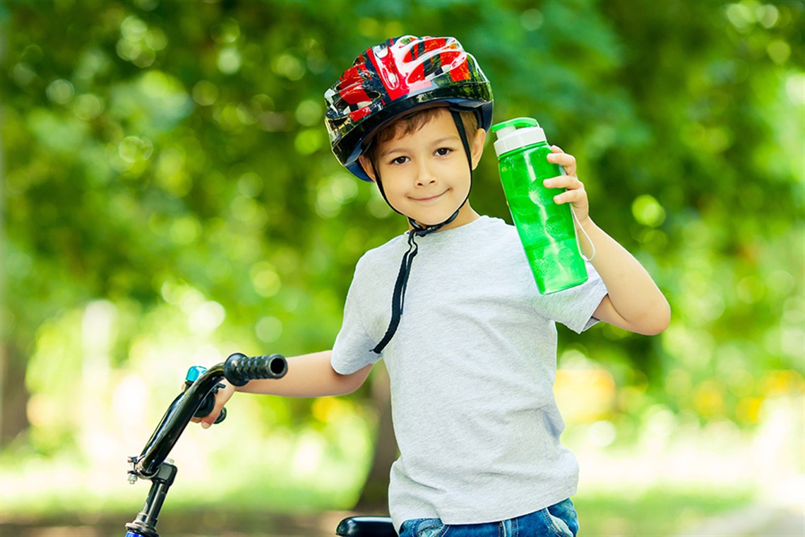 Young boy with a bicycle, safety helmet, holding a water bottle