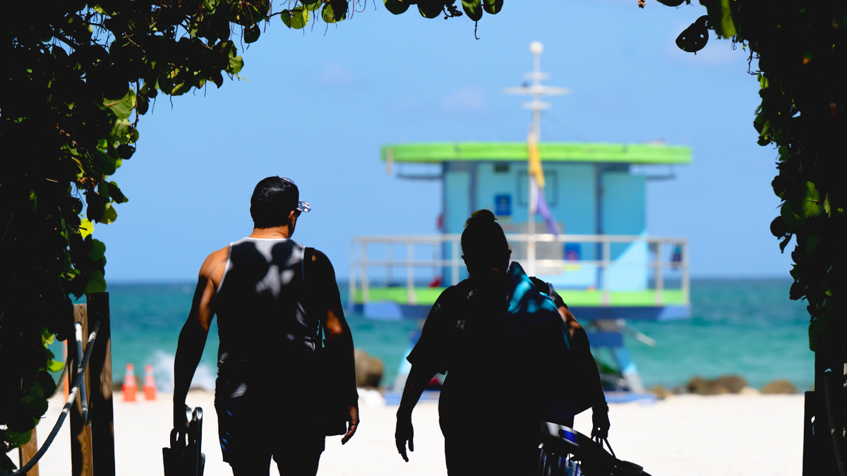Two people are seen walking to the beach in Miami, Florida on June 19, 2025.