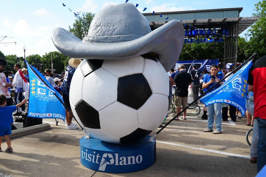 A giant soccer ball with a cowboy hat on top and blue flags either side. 