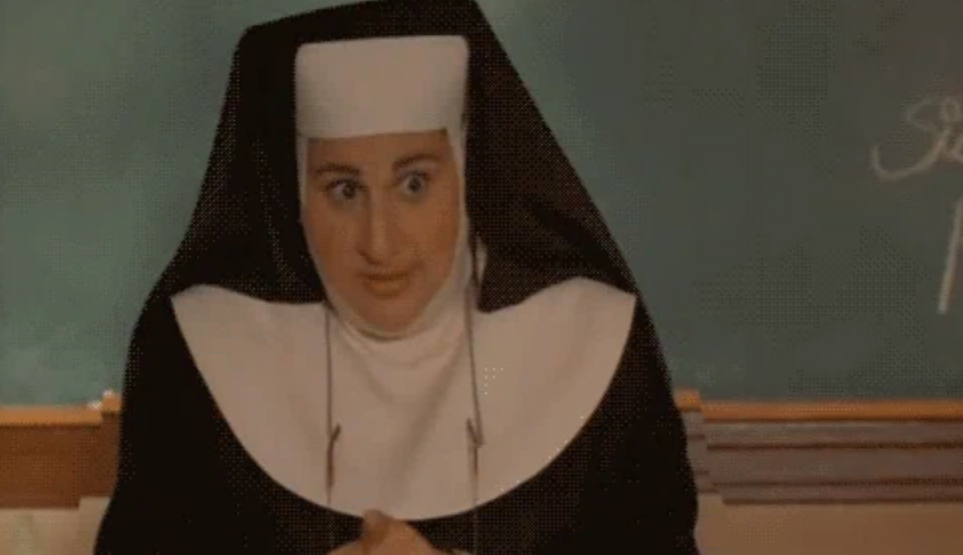 A person dressed as a nun stands in front of a chalkboard with a playful expression
