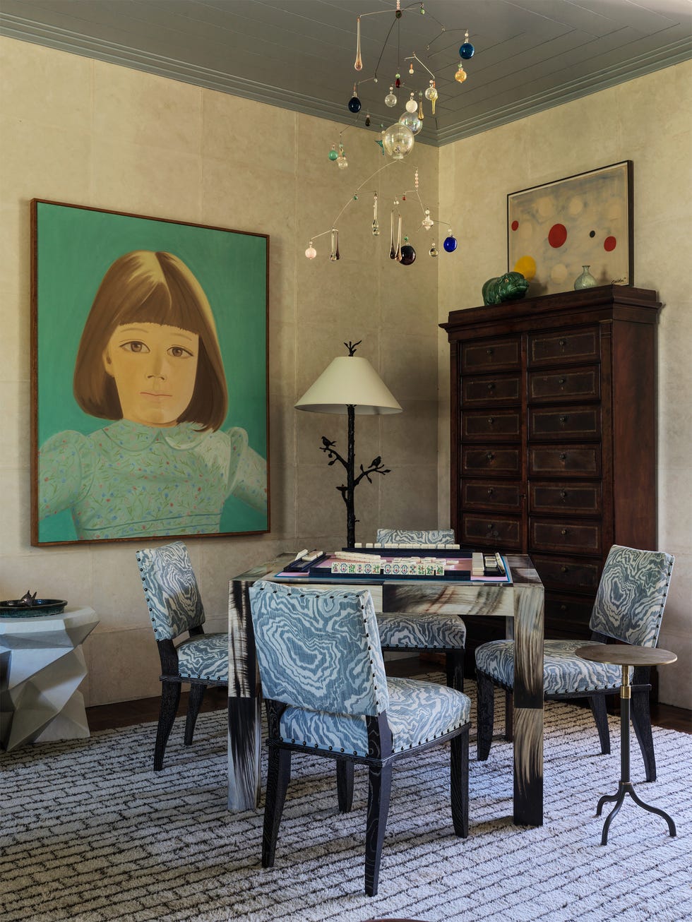 Cozy room with four blue-patterned chairs, a modern table, large child portrait, abstract wall art, and a decorative mobile.