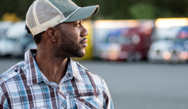 A picture of a truck driver at a truck stop in front of trucks.