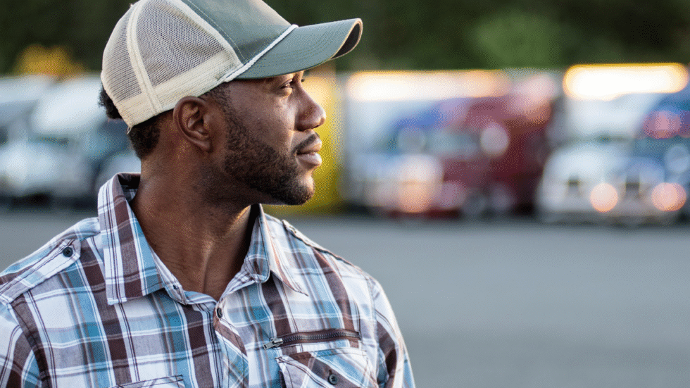 A picture of a truck driver at a truck stop in front of trucks.