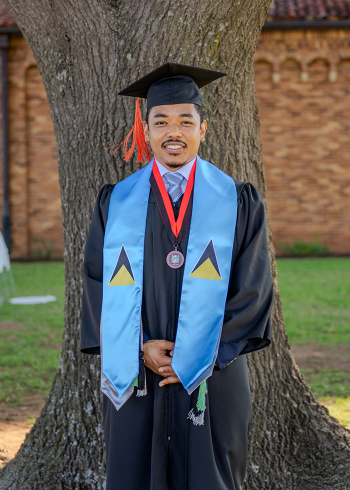 Joshua Muroi stands beside tree after his graduation