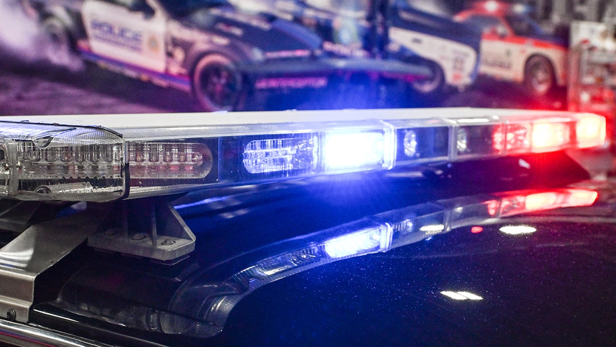Close-up of flashing red and blue police lights on the roof of a patrol vehicle with emergency vehicles visible in the background.