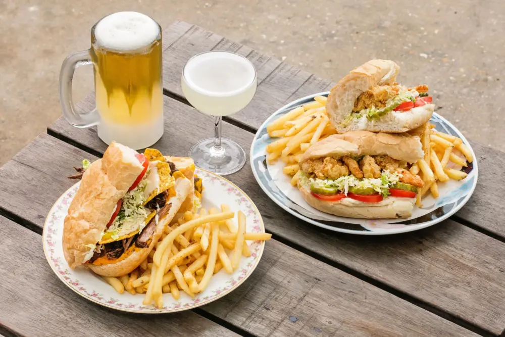 Photo of po'boys with fries alongside beer and a daquiri