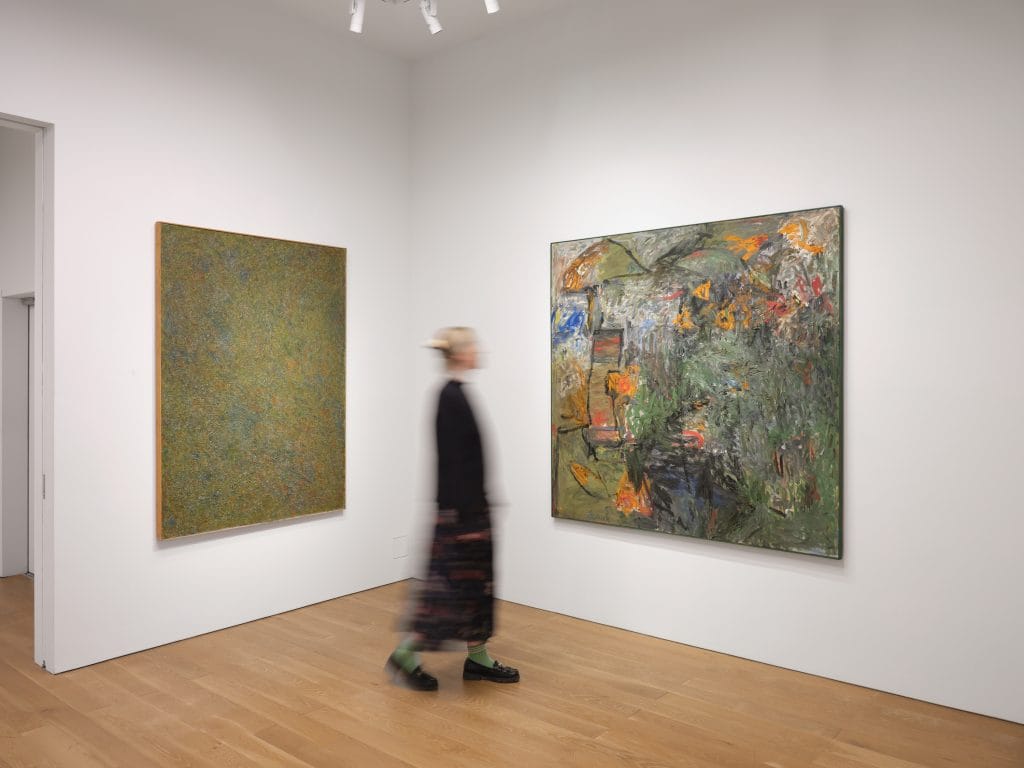Gallery installation featuring two large abstract paintings on white walls, blurred visitor passing.