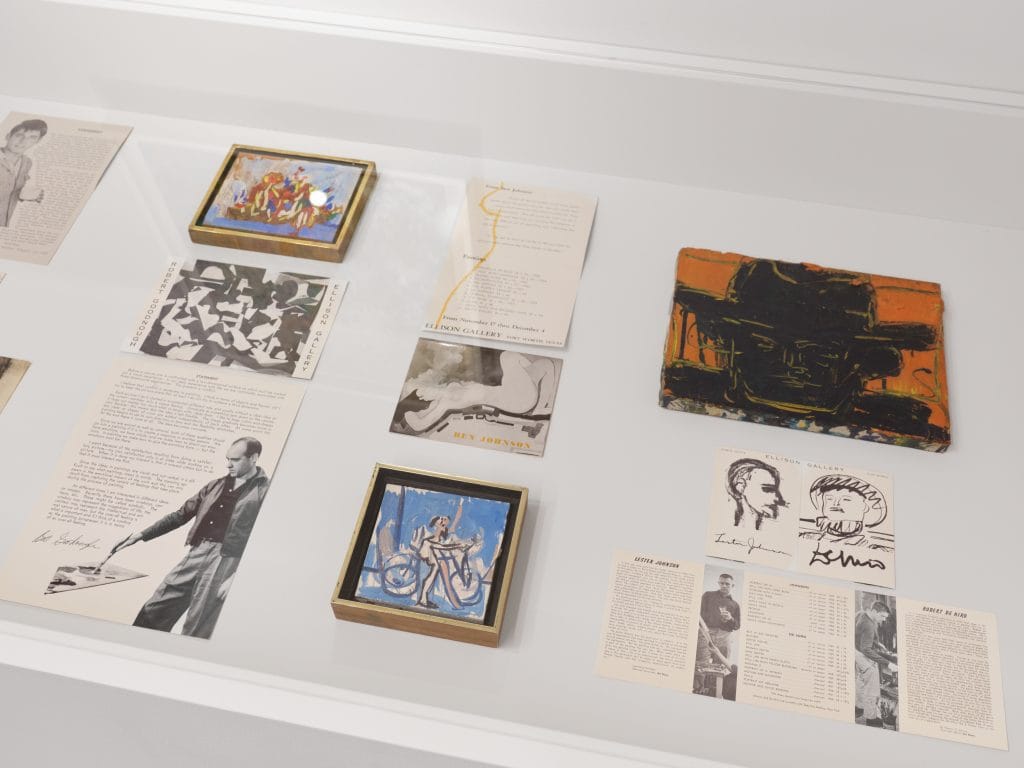 Display case containing artworks, exhibition invitations, photographs, and archival documents from artists.
