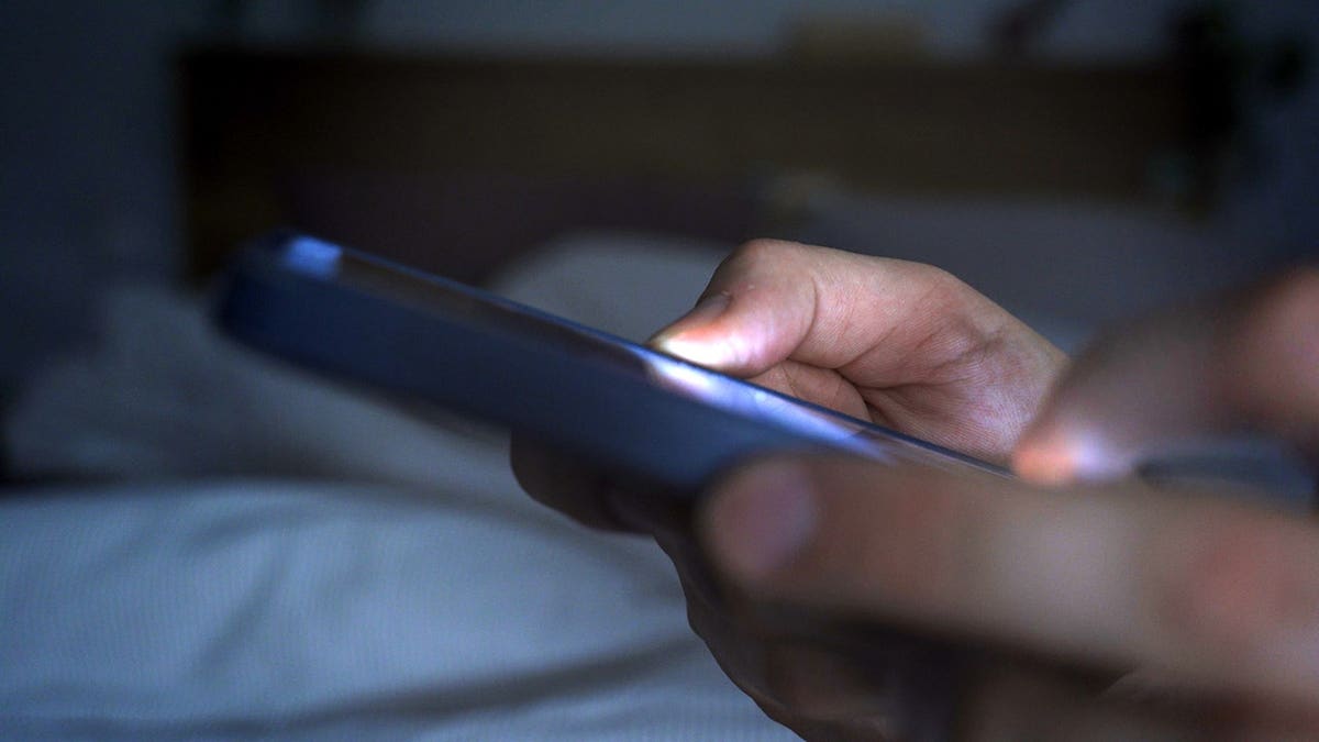 Hands holding and using a smartphone in bed at night
