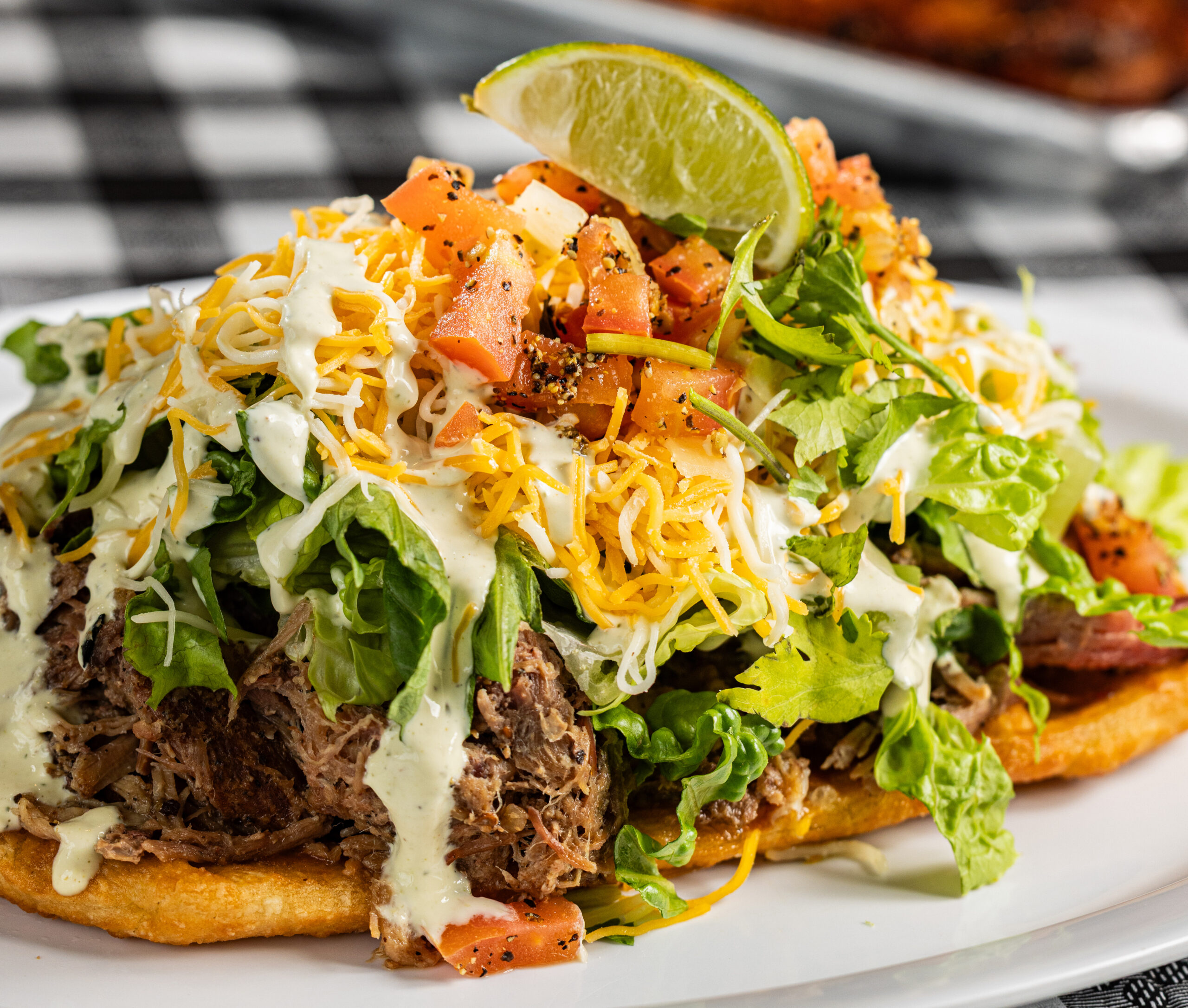 Navajo fry bread tacos contain “Burnt” pinto beans, choice of barbecue meat, chopped romaine, cheddar jack cheese, avocado lime crema, pico, cilantro and lime. Photography by Kathy Tran