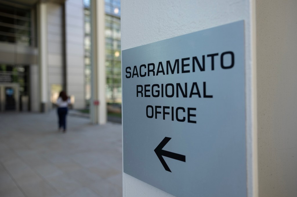 A grey sigh that reads "Sacramento Regional Office, with a black arrow underneath. Out of focus in the background is a person walking through an office building corridor.