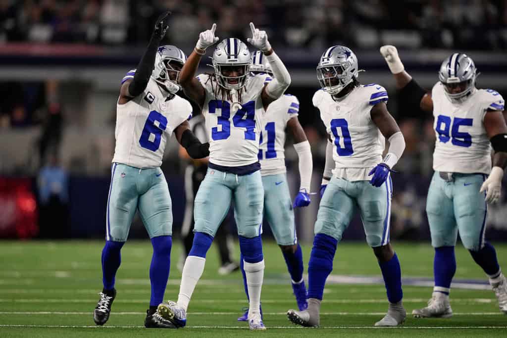 Dallas Cowboys defenders Donovan Wilson, Shevon Revel Jr, DeMarvion Overshown, and Kenny Clark celebrate together on the field.
