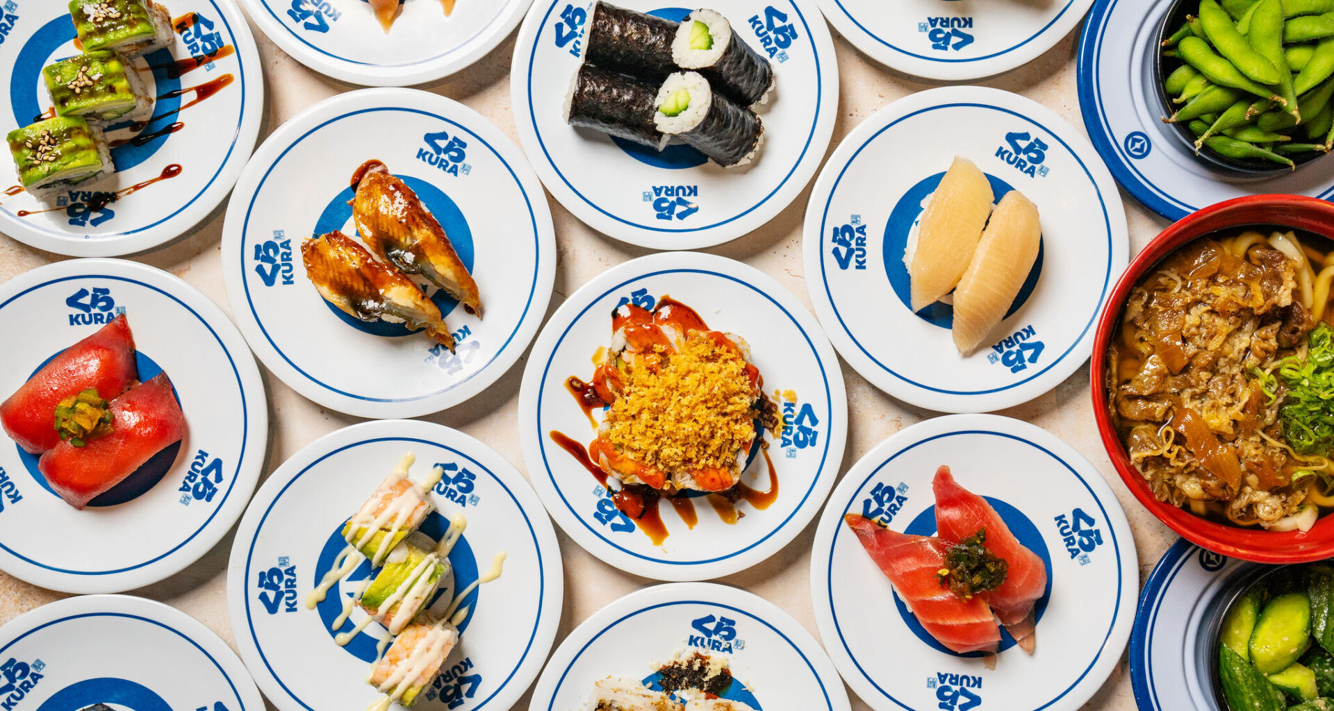 A hand grabs sushi being served on a conveyor belt at Kura Revolving Sushi Bar. 