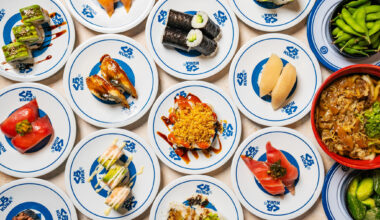 A hand grabs sushi being served on a conveyor belt at Kura Revolving Sushi Bar. 