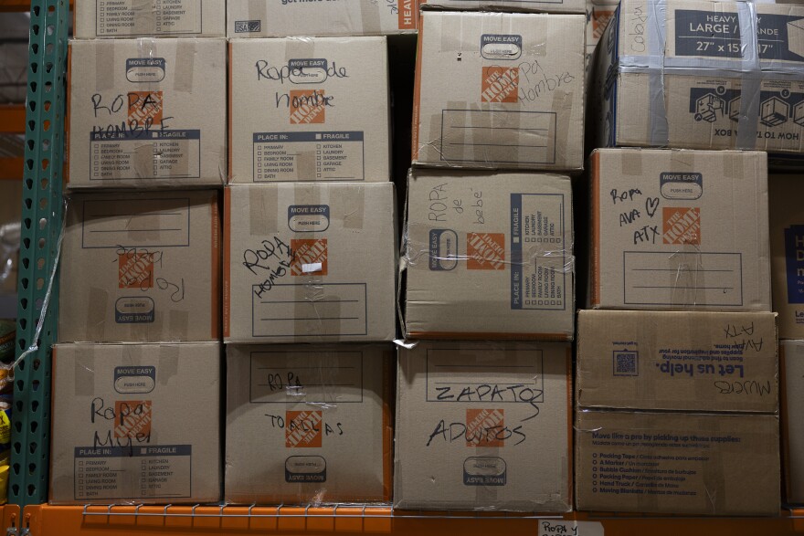 Boxes sit on an orange shelf in a warehouse with writing on the front of them.