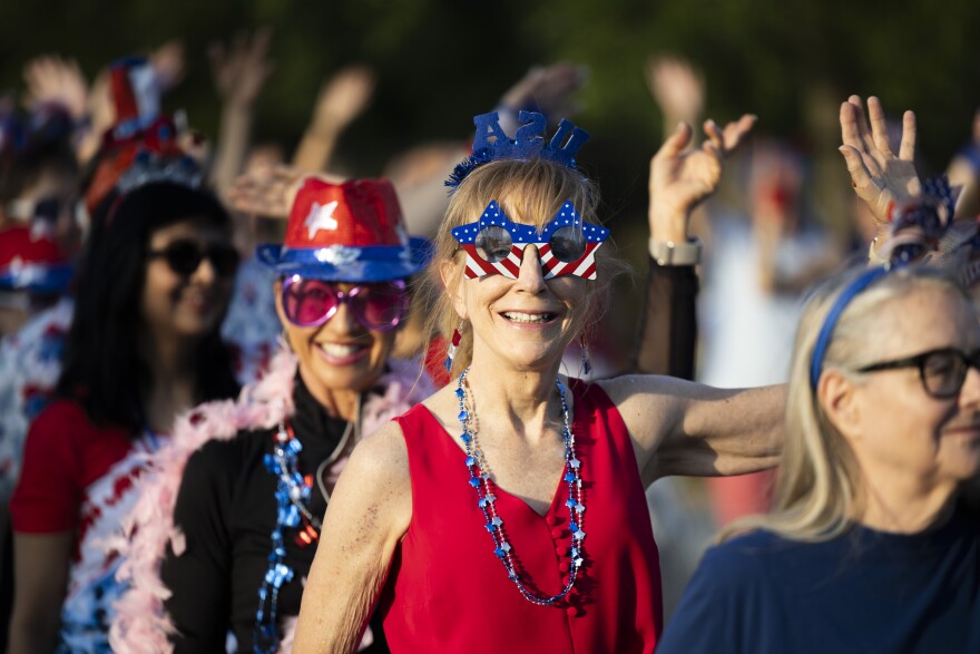 A group of women wearing patriotic attire wave.