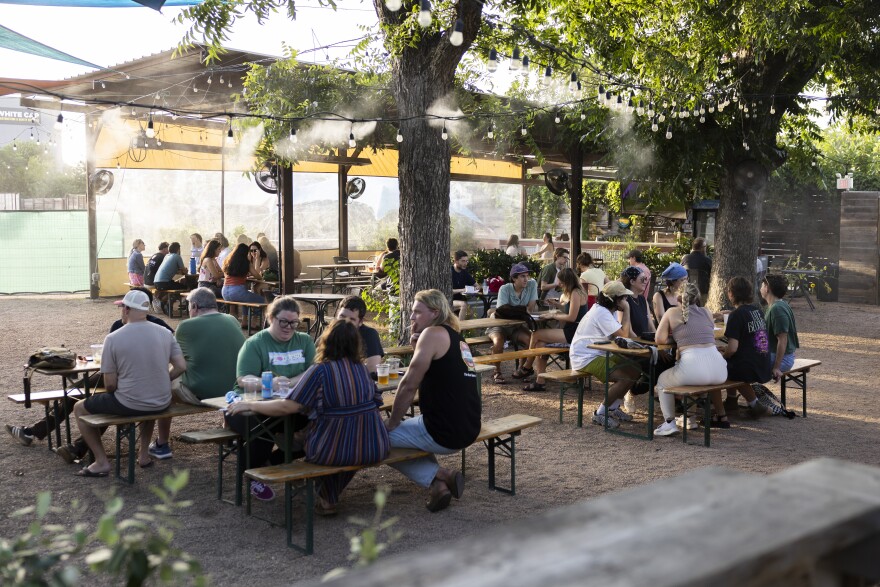 People sit at picnic tables at an outdoor bar.