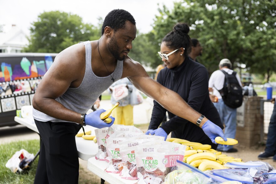 A man wearing gloves organizes bananas and other produce on a table outside.
