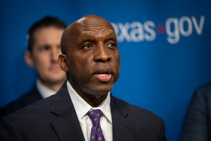 A man is shown at a press conference wearing a suit.