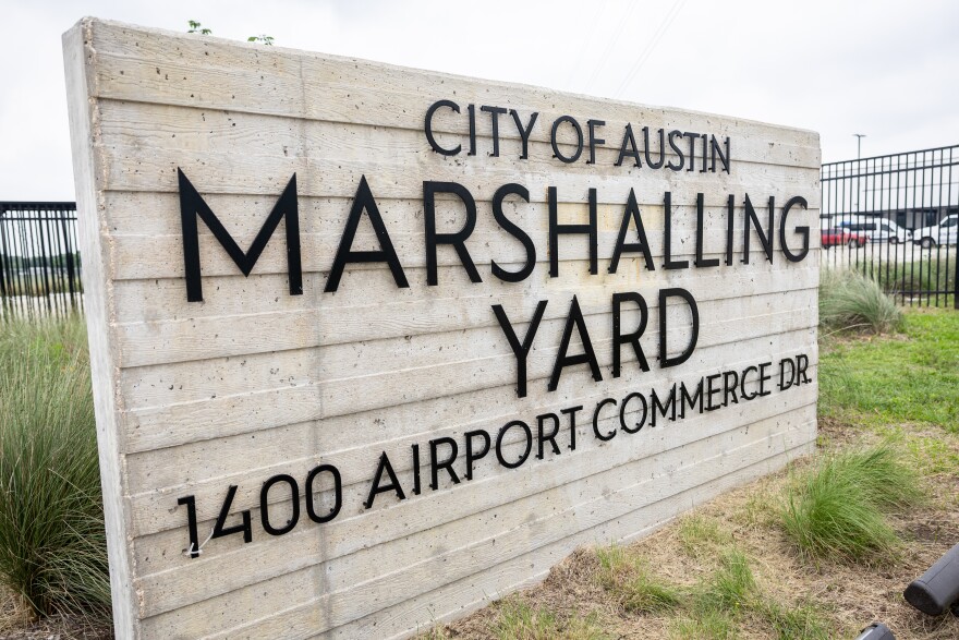 A large concrete sign with the words City of Austin Marshalling Yard and address 1400 Airport Commerce Dr., is shown sitting outside near a large metal fence.