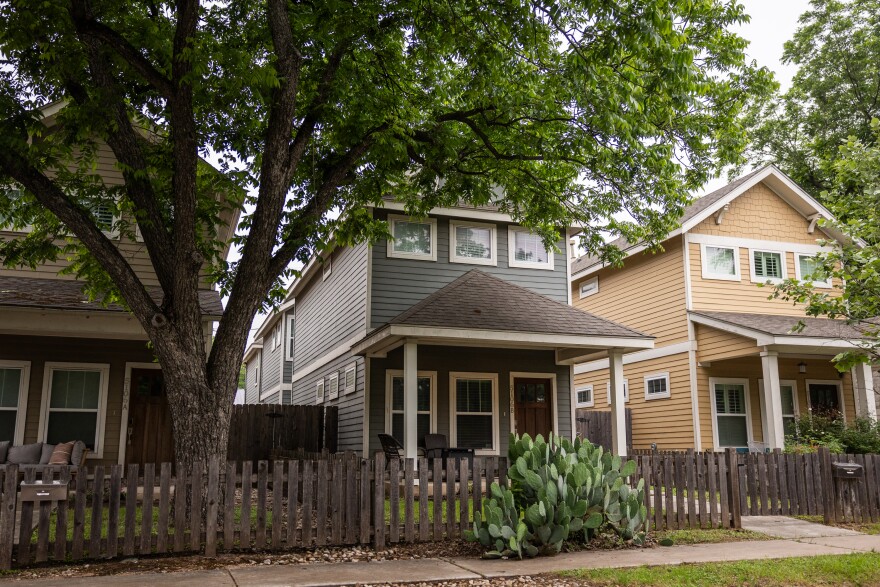 Two story homes are shown on a street with a tree.