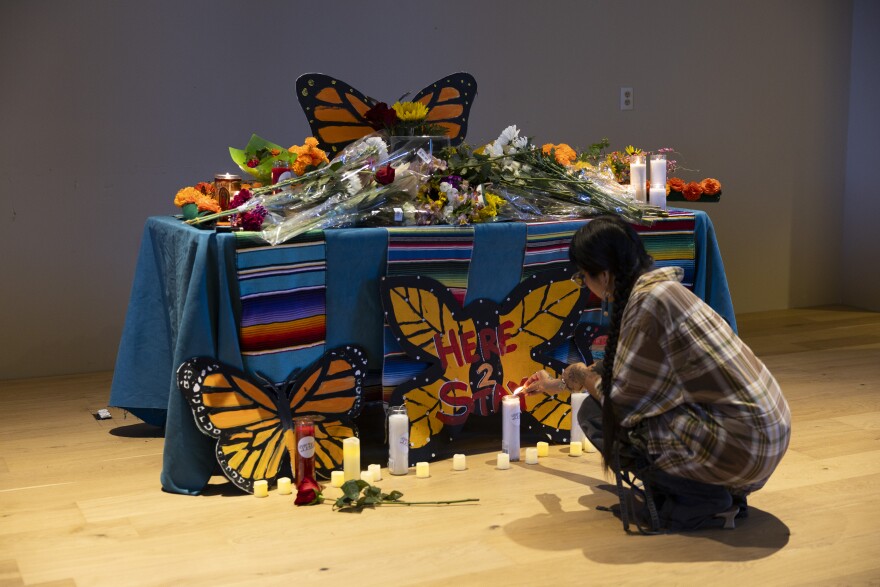 A person kneels to light a candle in front of a shrine for Lorenzo Salgado Araujo decorated with flowers, a photo, and illustrations of monarch butterflies.