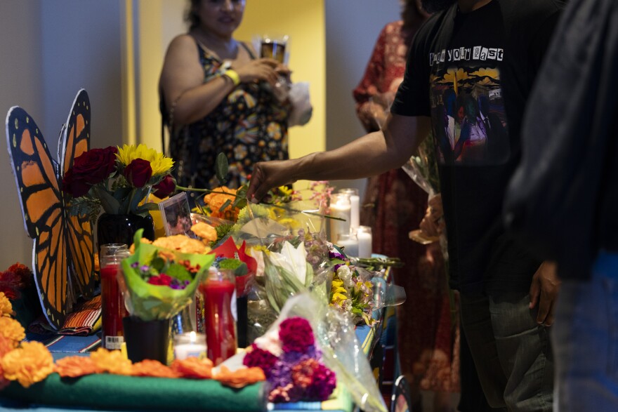 A line of people lay flowers on a memorial shrine decorated with monarch butterflies and marigolds.