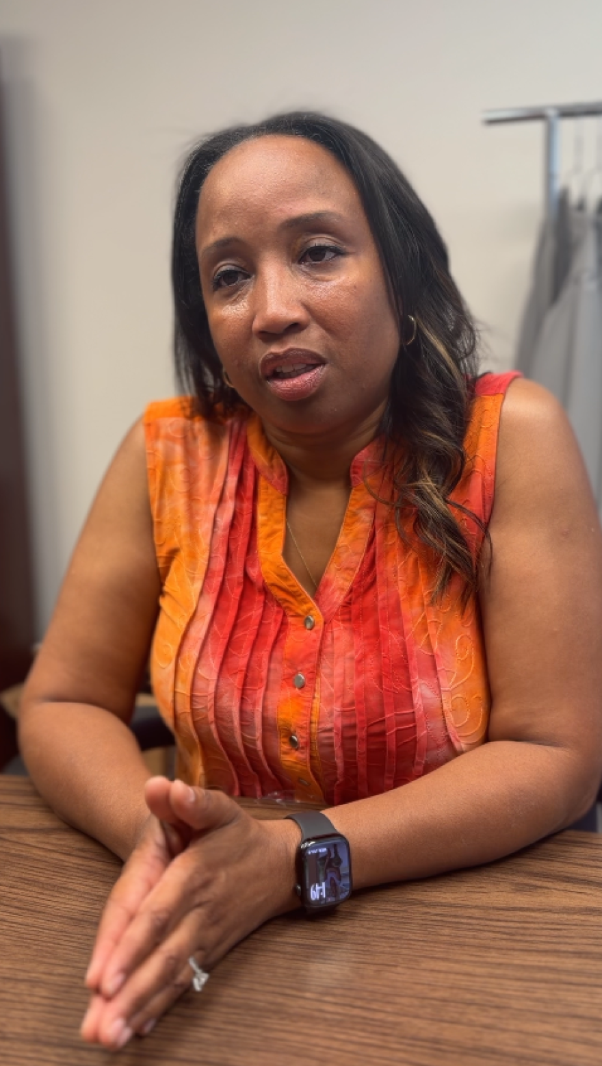 A woman in an orange shirt is seated at a table inside a conference room. 