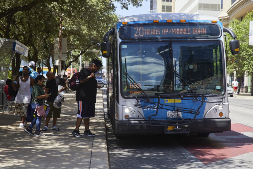 People line up to board CapMetro bus #20 on Guadalupe Street. The destination sign on the front of the bus says, "20 Heads Up/Phones Down."